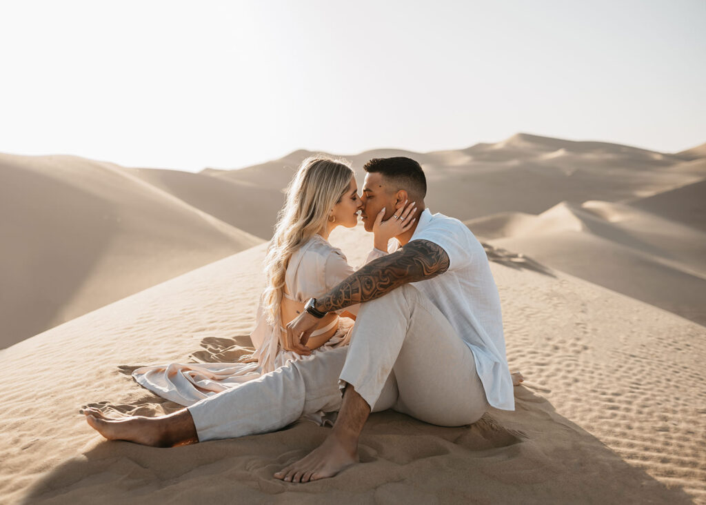 couple kissing at the sand dunes during their engagement session.